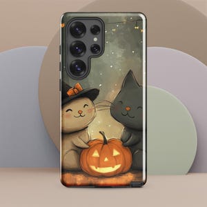 Puede incluir: Una funda para teléfono con temática de Halloween con dos gatos, uno con un sombrero de bruja, y una calabaza tallada. La funda tiene un fondo oscuro con un efecto de brillo sutil.