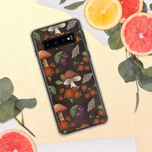 Puede incluir: Una funda transparente para teléfono con fondo marrón oscuro y un patrón repetitivo de setas, mariposas y flores. La funda tiene un recorte para la lente de la cámara del teléfono.
