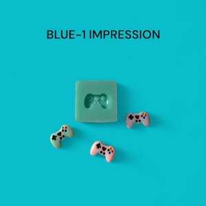 May include: A blue silicone mold shaped like a video game controller. Three small, colorful, resin-cast video game controllers are on a blue background. The text "BLUE-1 IMPRESSION" is at the top of the image.