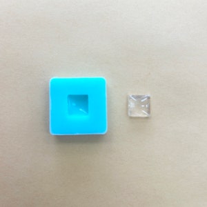 May include: A light blue silicone mold with a square-shaped cavity. Next to the mold is a clear square-shaped resin piece.