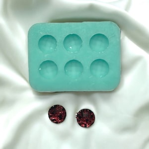 May include: A turquoise silicone mold with six round cavities, used for making resin earrings. Two red glitter resin earrings are shown next to the mold.