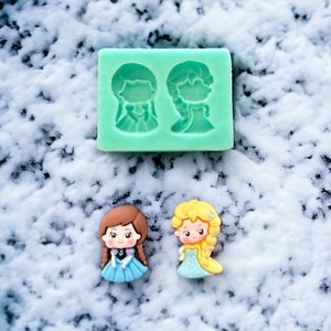 May include: Two silicone molds for making small figurines of two girls with long hair. One mold is for a girl with brown hair and a blue dress, the other is for a girl with blonde hair and a blue dress.