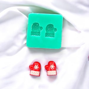 May include: Two red and white Christmas mitten ornaments with a snowflake design. A green silicone mould with two mitten shapes is also shown.