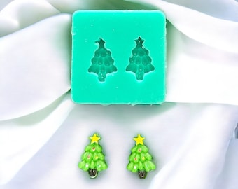 May include: A green silicone mould with two Christmas tree shapes. Two green Christmas tree ornaments with yellow stars are shown next to the mould.