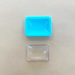 May include: A light blue silicone mold and a clear glass rectangle. The mold is for making a rectangular shaped object.