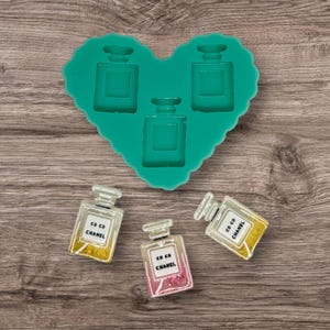 Peut inclure: Un moule en silicone en forme de cœur vert avec trois formes de flacons de parfum. Il y a trois flacons de parfum remplis avec le texte "CO CO CHANEL" dessus. Deux flacons sont jaunes et dorés, et un est rose et doré.