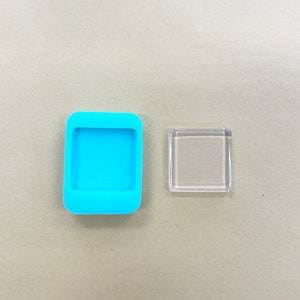 May include: A blue silicone mold and a clear glass square, both for crafting resin jewelry.