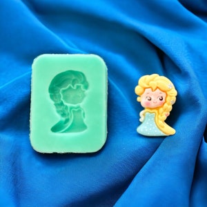 May include: A green silicone mold with a raised design of a cartoon princess with long blonde hair. A small, yellow, blue, and white cartoon princess figurine is next to the mold.