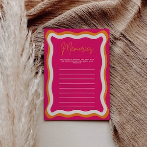May include: A pink card with a wavy orange border and white text that reads "Memories". The text below the title says "Write down a memory you have with the bride and she will guess who wrote it."