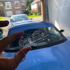 Peut inclure: Un porte-clés en acrylique transparent avec un contour noir et blanc d'une voiture et le texte "Everything comes in waves".