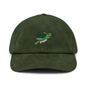 May include: A green corduroy baseball cap featuring an embroidered image of a smiling sea turtle.