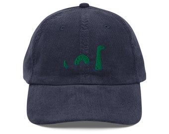 May include: A navy blue corduroy baseball cap with an embroidered green Nessie, the Loch Ness Monster, on the front.