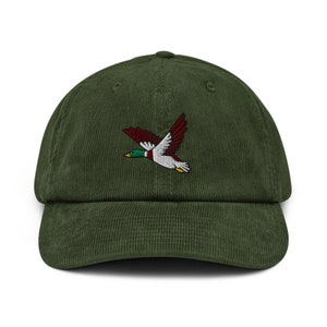 May include: A green corduroy baseball cap with an embroidered image of a flying duck with red, white, and green accents.