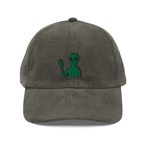Puede incluir: Una gorra de béisbol de pana verde oscuro con un extraterrestre verde bordado que saluda.