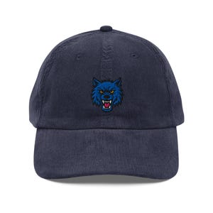 May include: Navy blue corduroy baseball cap featuring an embroidered blue wolf design. The wolf has a fierce expression with sharp teeth. The cap has a curved brim and an adjustable strap for a comfortable fit. A stylish accessory.