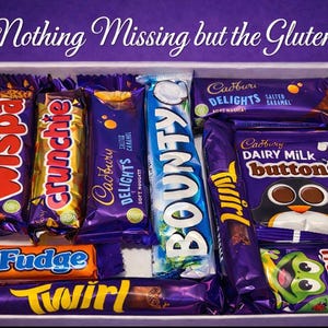 Może przedstawiać: Biała taca wypełniona różnymi batonami czekoladowymi i słodyczami Cadbury, w tym Wispa, Crunchie, Cadbury Delights, Bounty, Twirl, Fudge, Dairy Milk Buttons i Freddo. U góry znajduje się napis "Nothing Missing but the Gluten!".