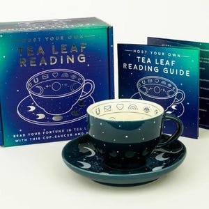 May include: A teal tea cup and saucer set with white polka dots, alongside a box and guide for tea leaf reading. The box and guide feature a celestial design with a teacup illustration and the text "HOST YOUR OWN TEA LEAF READING".