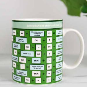 Peut inclure: Une tasse en céramique verte avec une poignée blanche. La tasse a une bordure blanche et un fond vert avec du texte blanc qui dit "Spreadsheet shortcut mug". Le texte est disposé en grille avec des raccourcis clavier pour Microsoft Excel.