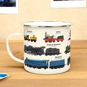 May include: White enamel mug featuring a colourful illustration of famous trains from around the world. The trains include the Rocket, Adler, Orient Express, and Mallard. The mug has a white handle.