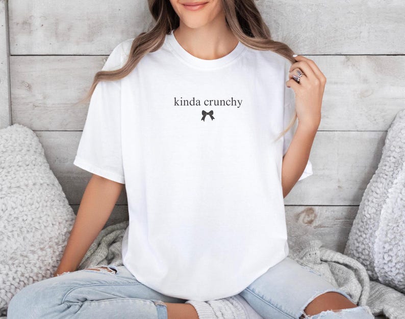 Op de afbeelding: Wit T-shirt met de tekst "kinda crunchy" en een klein zwart strikje.