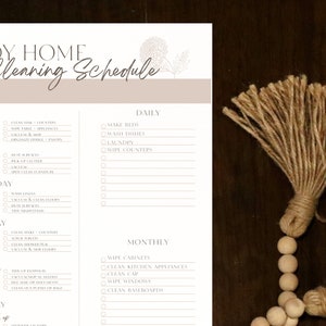 K&ouml;nnte beinhalten: Eine druckbare Checkliste f&uuml;r einen Reinigungsplan mit einem floralen Design. Die Checkliste enth&auml;lt t&auml;gliche, w&ouml;chentliche und monatliche Reinigungsaufgaben f&uuml;r K&uuml;che, Wohnzimmer, Badezimmer und das gesamte Haus. Der Text enth&auml;lt "Tidy Home Cleaning Schedule".
