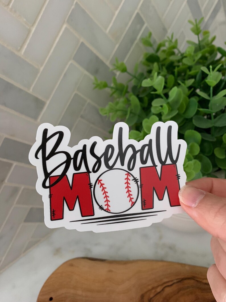 以下が含まれることがあります： 白地に黒文字で「Baseball Mom」と書かれたステッカー。中央には赤い野球ボールが描かれている。