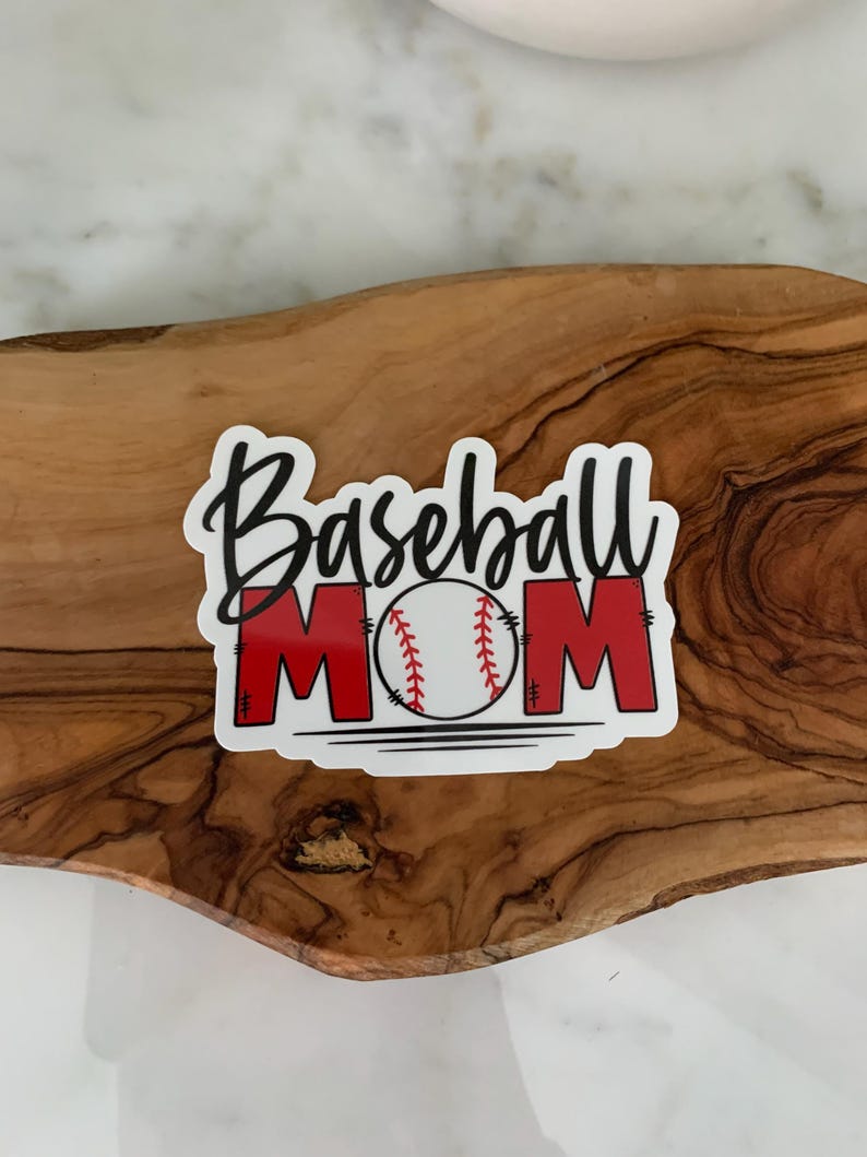 以下が含まれることがあります： 「Baseball Mom」という黒い文字と、中央に赤い野球のグラフィックが描かれた白いステッカーです。