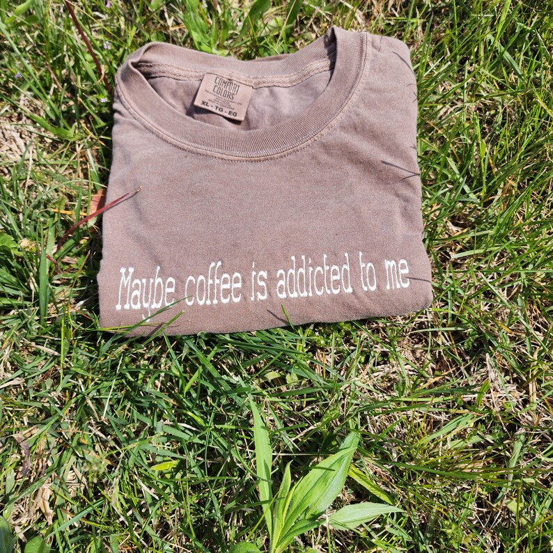 May include: A brown t-shirt with the text "Maybe coffee is addicted to me" embroidered in white on the front.