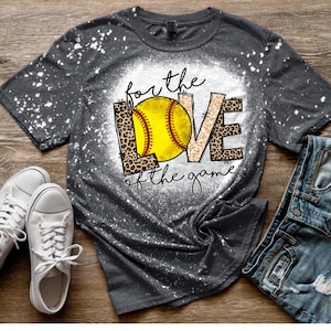 May include: A gray t-shirt with a bleach-splattered design. The shirt features a graphic of a softball with the words "for the love of the game" in a leopard print font.