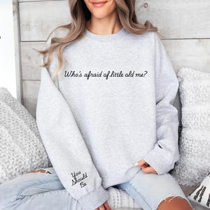 May include: A gray sweatshirt with the text "Who's afraid of little old me?" printed on the front. The text "You Should Be" is printed on the left sleeve.