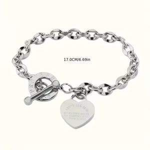 May include: A silver-toned bracelet with a toggle clasp and a heart-shaped charm. The bracelet is 6.69 inches (17.0 cm) long and features a chain link design. The heart charm has engraved text. The clasp has the word "PROTECT" engraved on it.