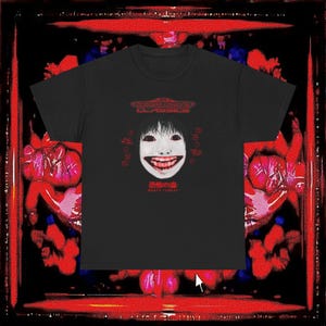 May include: Black t-shirt featuring a white, smiling face graphic with black hair and red accents. The shirt includes Japanese text and the words "DEATH FOREST" below the graphic. The shirt has the words "MEGA DRIVE CLASSICS" at the top.