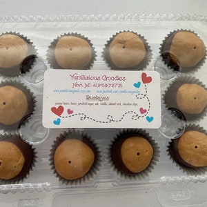May include: A clear plastic container filled with 10 chocolate peanut butter candies called "Buckeyes". The candies are arranged in two rows of five. The container has a white label with the business name "Yumilicious Goodies" and contact information.