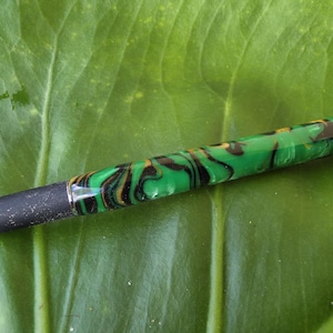 May include: A ballpoint pen featuring a cylindrical barrel with a marbled pattern of green, black, and gold swirls. The pen has a silver-toned metal cap at the top, a black grip section near the tip, and a silver-toned metal tip with a gold-colored point.
