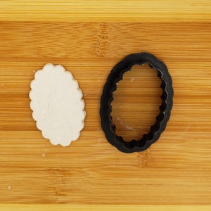May include: A black plastic oval cookie cutter and a white oval cookie on a wooden cutting board.