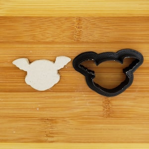 May include: A white cookie cutter in the shape of a bat with wings and a black plastic cookie cutter in the shape of a bat with wings.