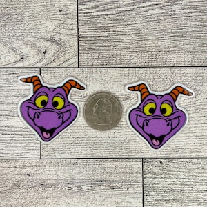 May include: Two purple and orange cartoon dragon faces with yellow eyes and a toothy grin. The dragon faces are on a white background.