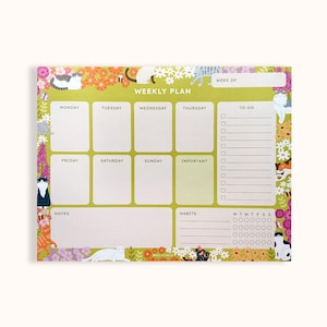 May include: A rectangular weekly planner notepad with a light green background, featuring floral borders and illustrations of various cats. The layout includes sections for Monday through Sunday, a to-do list, notes, and a habit tracker with checkboxes.