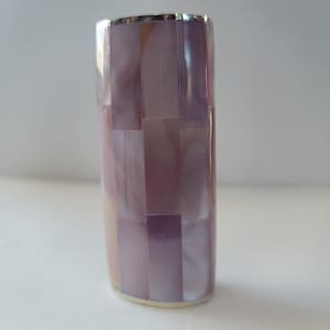 May include: A rectangular, iridescent, decorative object with a mosaic pattern of rectangular tiles in shades of lavender, pink, and white. The top edge is trimmed with a silver-colored metal. The object has a rounded base.