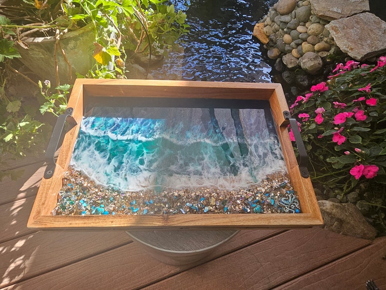 May include: A wooden serving tray with a resin inlay depicting a beach scene with blue and white waves crashing on a sandy shore. The resin is embedded with small blue and gold glitter.