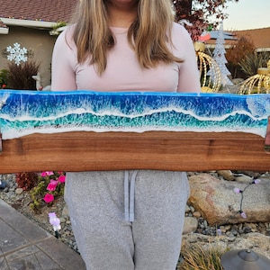 Könnte beinhalten: Ein Holztablett mit einem Design aus blauen und weißen Epoxy-Harz-Ozeanwellen. Das Tablett hat zwei Griffe an den Seiten.