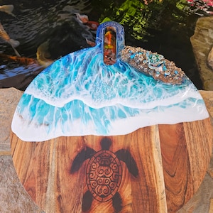 Puede incluir: Tabla de servir redonda de madera con un diseño de ola de océano de resina azul y blanca y una silueta de tortuga marina. La tabla tiene un asa y es perfecta para servir aperitivos o queso.