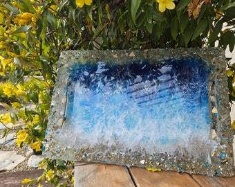 May include: A rectangular serving tray with a blue and white resin ocean wave design. The tray is surrounded by a border of small, glittery stones.