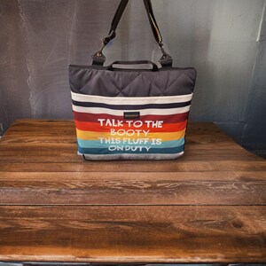 May include: A black quilted tote bag with a rainbow striped design and the text "Talk to the booty this fluff is on duty".