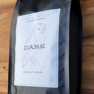 May include: Black coffee bag with a white label featuring a drawing of an owl and the text "Spice Theory Coffee Company" and "Dark Specialty Blend".