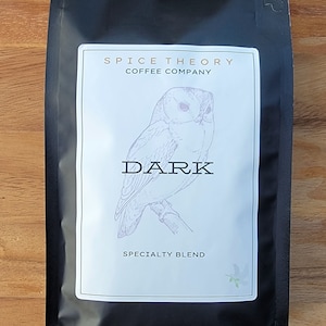 May include: Black coffee bag with a white label featuring a drawing of an owl and the text "Spice Theory Coffee Company" and "Dark Specialty Blend".