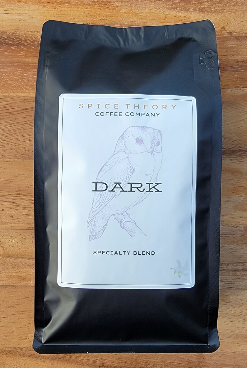 May include: Black coffee bag with a white label featuring a drawing of an owl and the text "Spice Theory Coffee Company" and "Dark Specialty Blend".