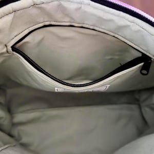 May include: Interior view of a tote bag with a zippered pocket. The bag's interior is a light green color, and the pocket has a black zipper. The bag's exterior is a mix of colors, including pink, purple, and yellow.