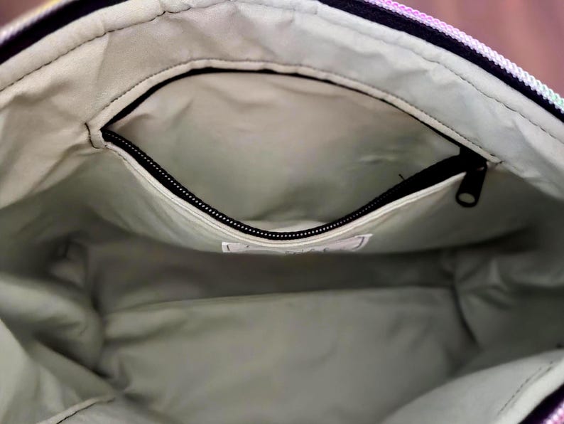 May include: Interior view of a tote bag with a zippered pocket. The bag's interior is a light green color, and the pocket has a black zipper. The bag's exterior is a mix of colors, including pink, purple, and yellow.