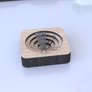 Może przedstawiać: Drewniany organizer biurkowy z małym przegrodą na spinacze. Przegroda ma okrągły kształt z koncentrycznymi pierścieniami.